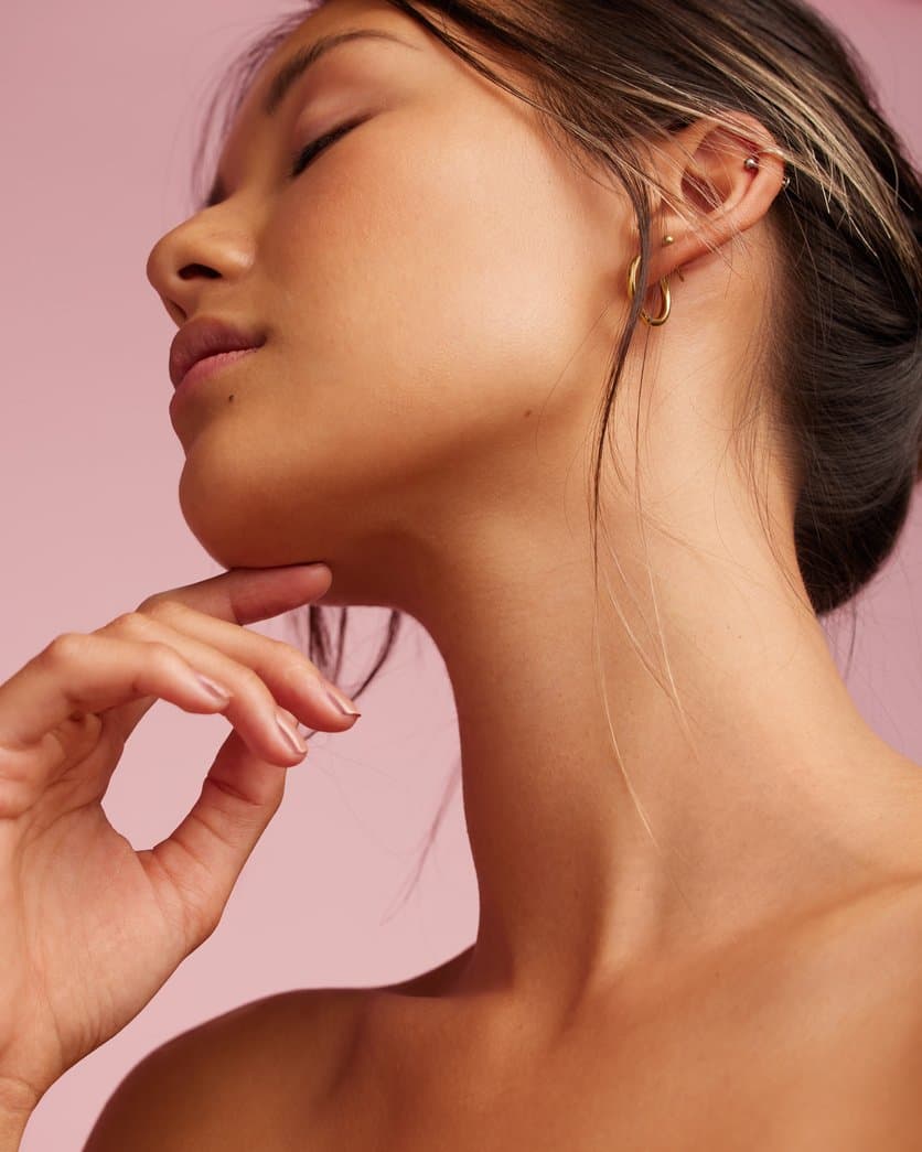 Woman with smooth, glowing skin along her jawline and neck, her fingertips at her chin — Glowtober at Neoderma Anaheim